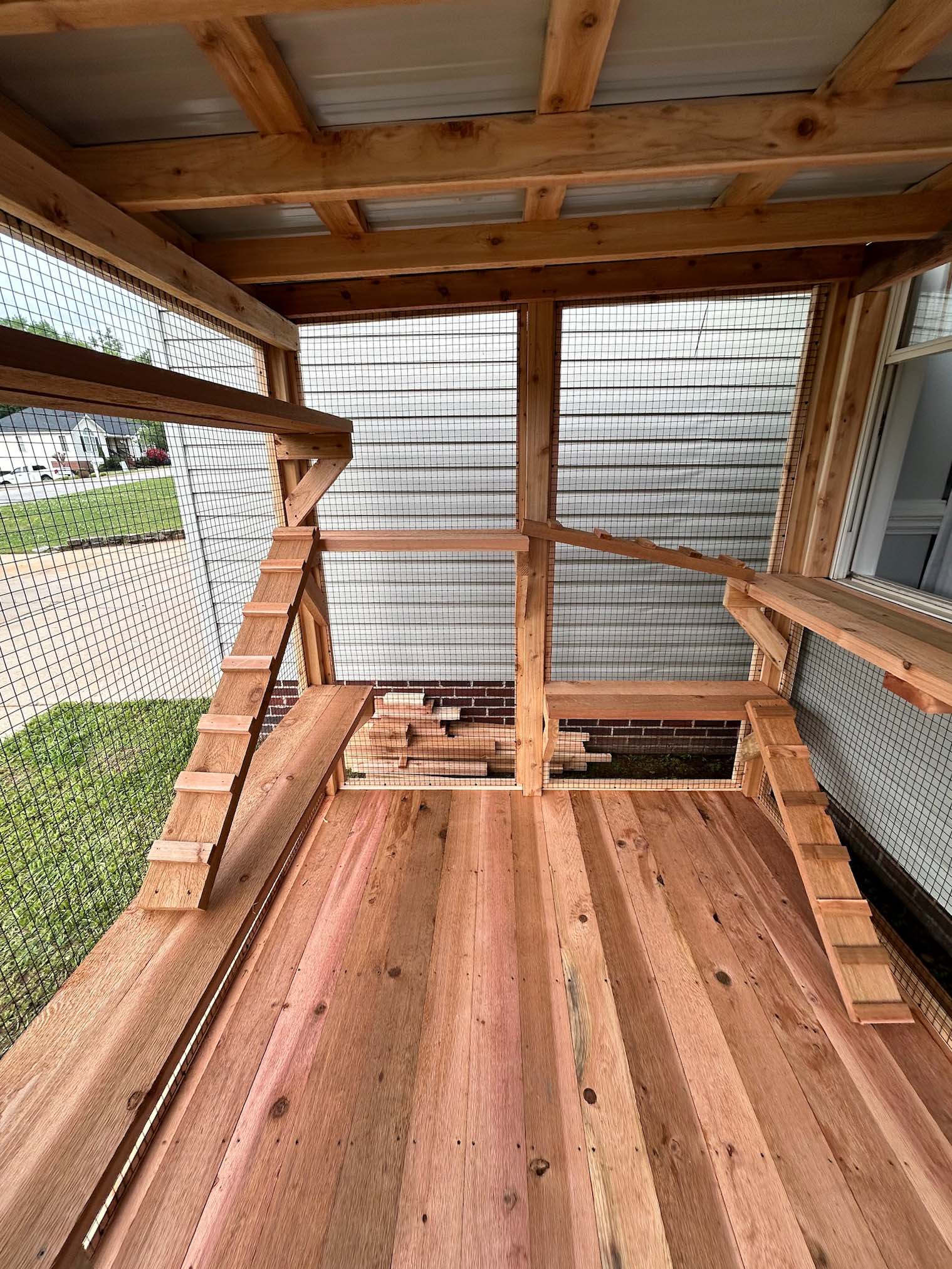 Interior view of a custom wooden catio with multiple ramps and shelves, built with smooth natural wood flooring and enclosed by wire mesh walls.
