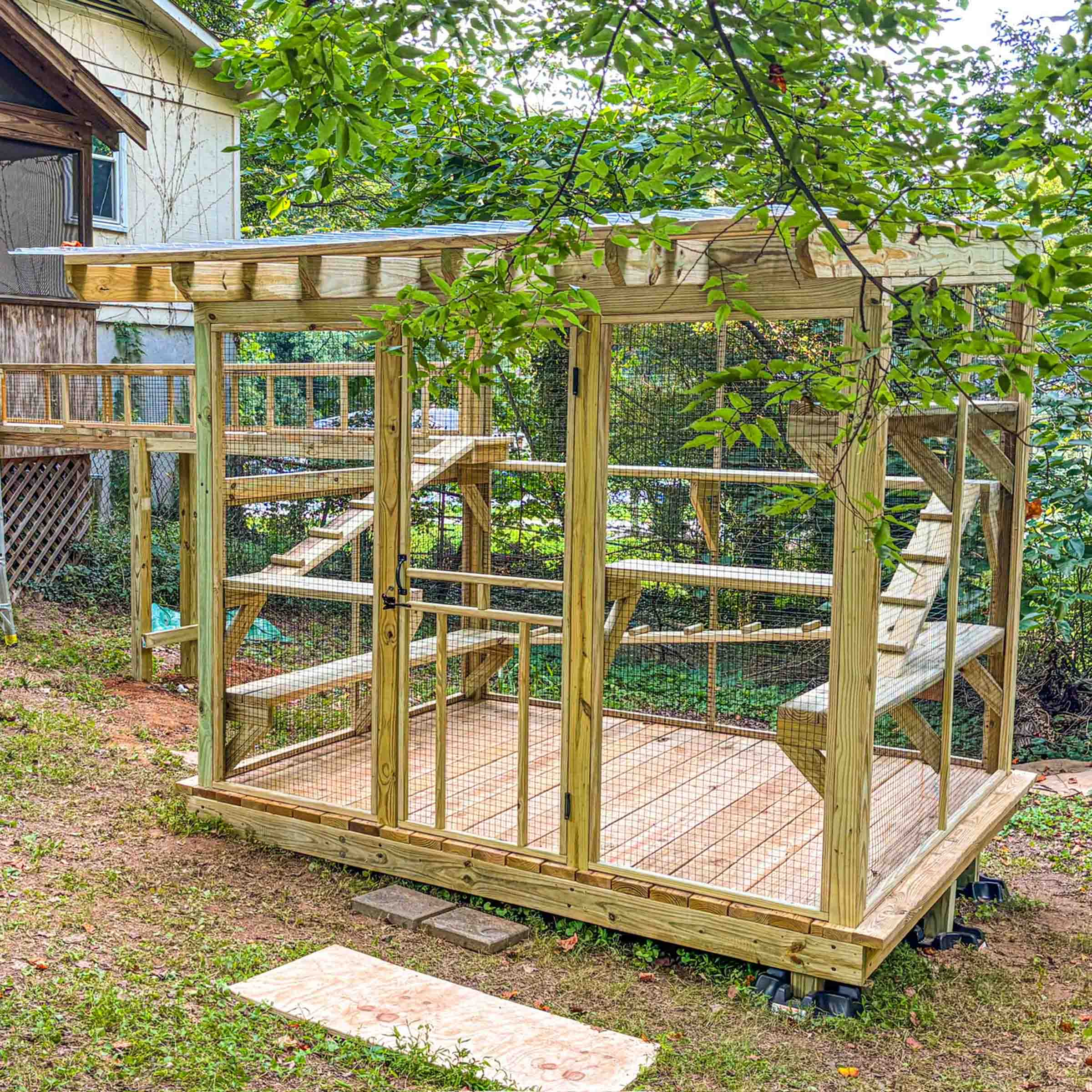 Custom-built catio with wood framing, multiple perches, and an access tunnel leading to the house.