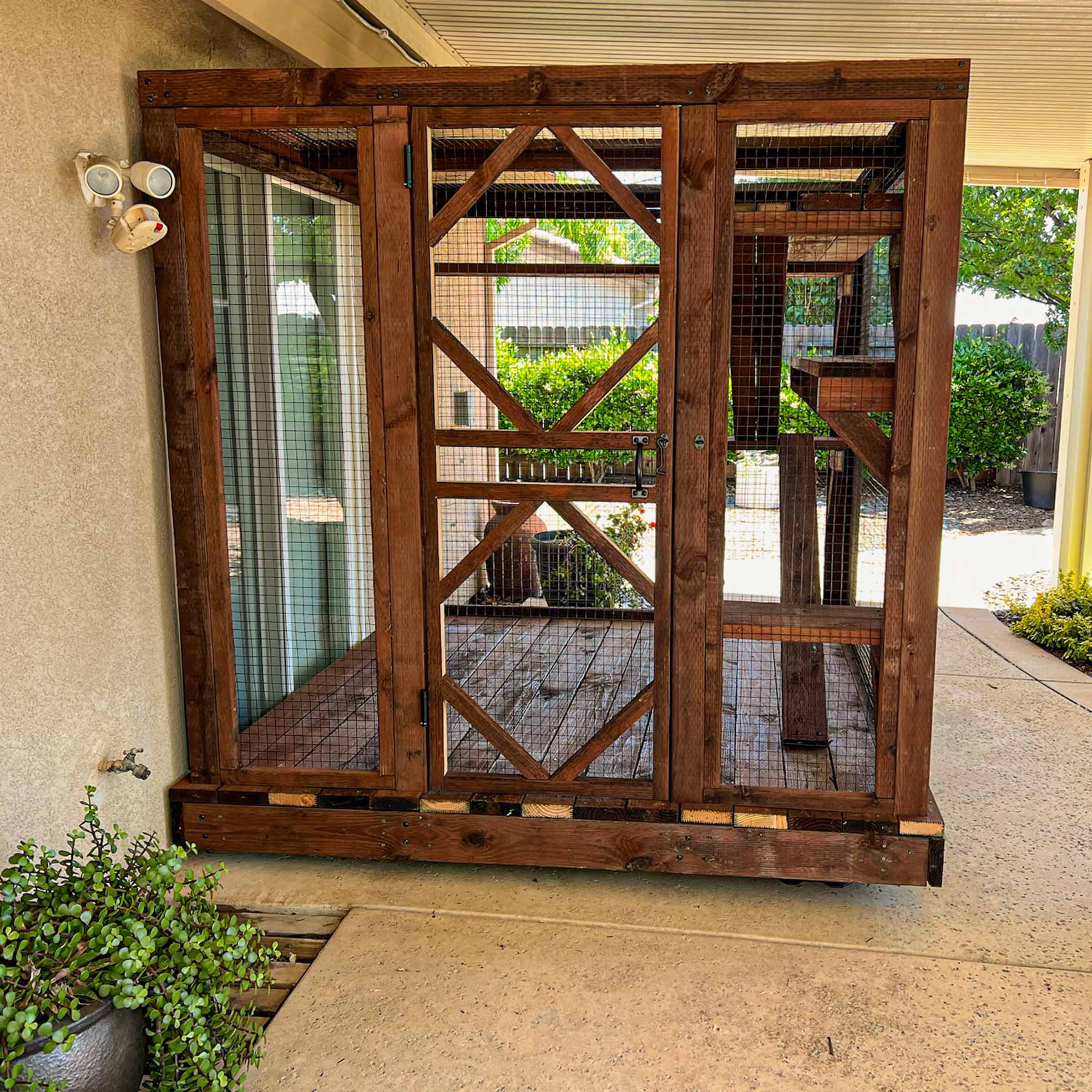 Front view of a custom wooden catio enclosure with a secure decorative door and enclosed platforms.