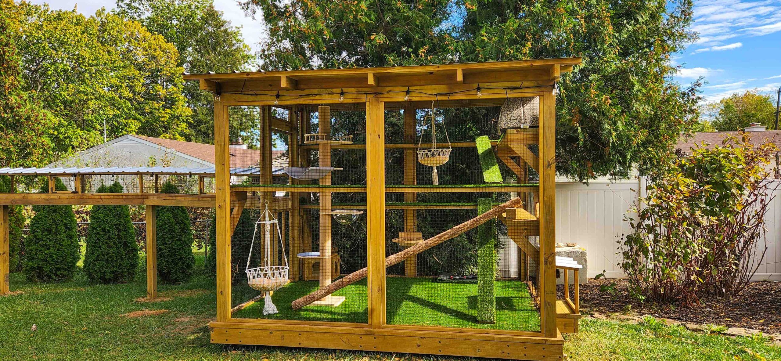 Large outdoor wooden catio with multiple climbing levels, hammocks, and a connecting tunnel leading from the house.