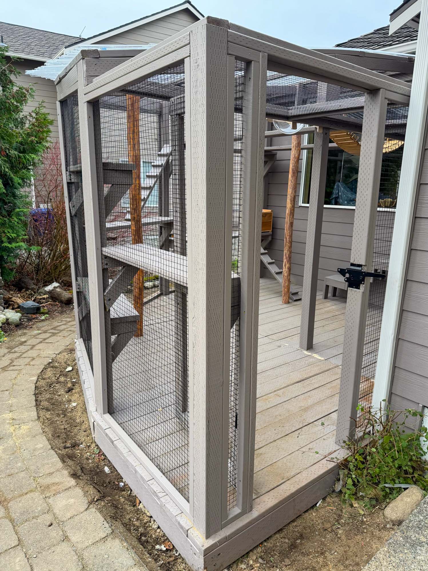 Side entry of a catio with wire mesh panels and visible shelves leading into the main enclosure.