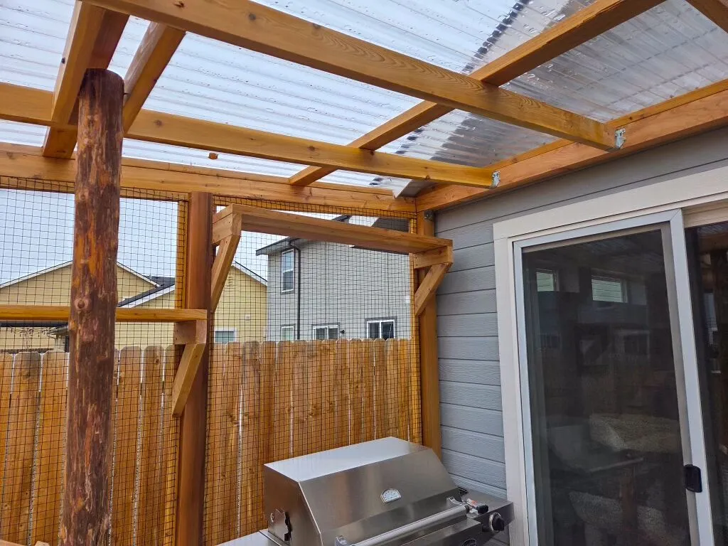 Corner of the catio attached to home exterior showing roof framing and screened panels.