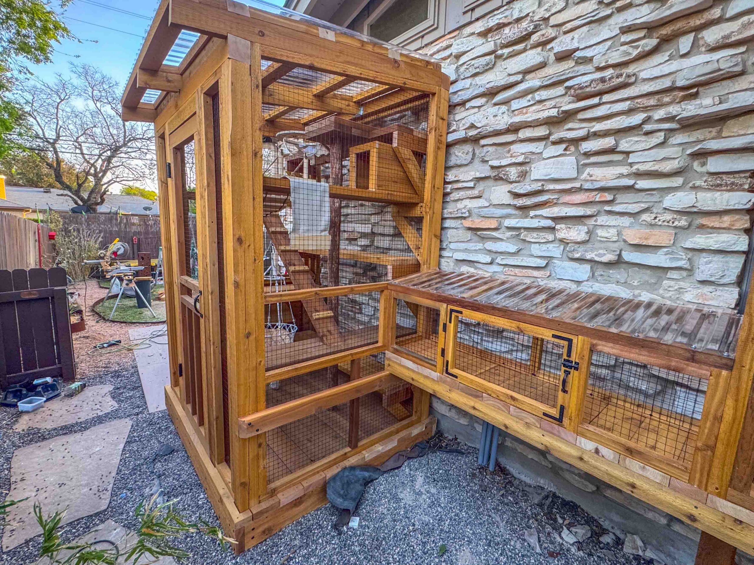 Angled view of a custom catio extension connected to a window box enclosure with a slanted clear roof and secure mesh panels.