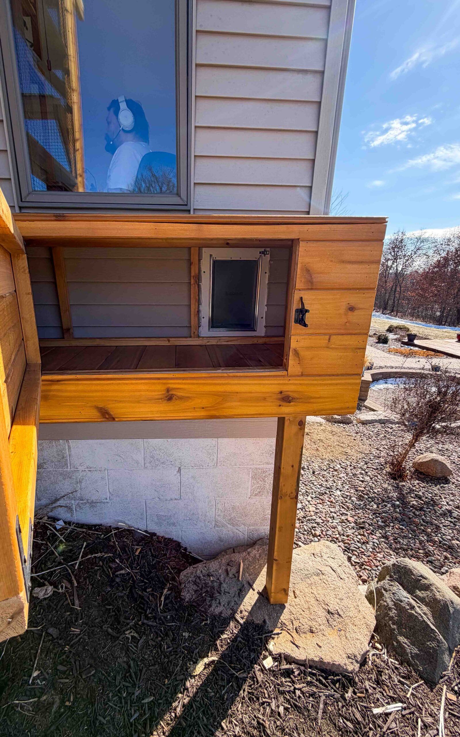 Wooden catio tunnel with a cat door connecting the house window to the outdoor enclosure, allowing cats safe and direct access from indoors to the catio.