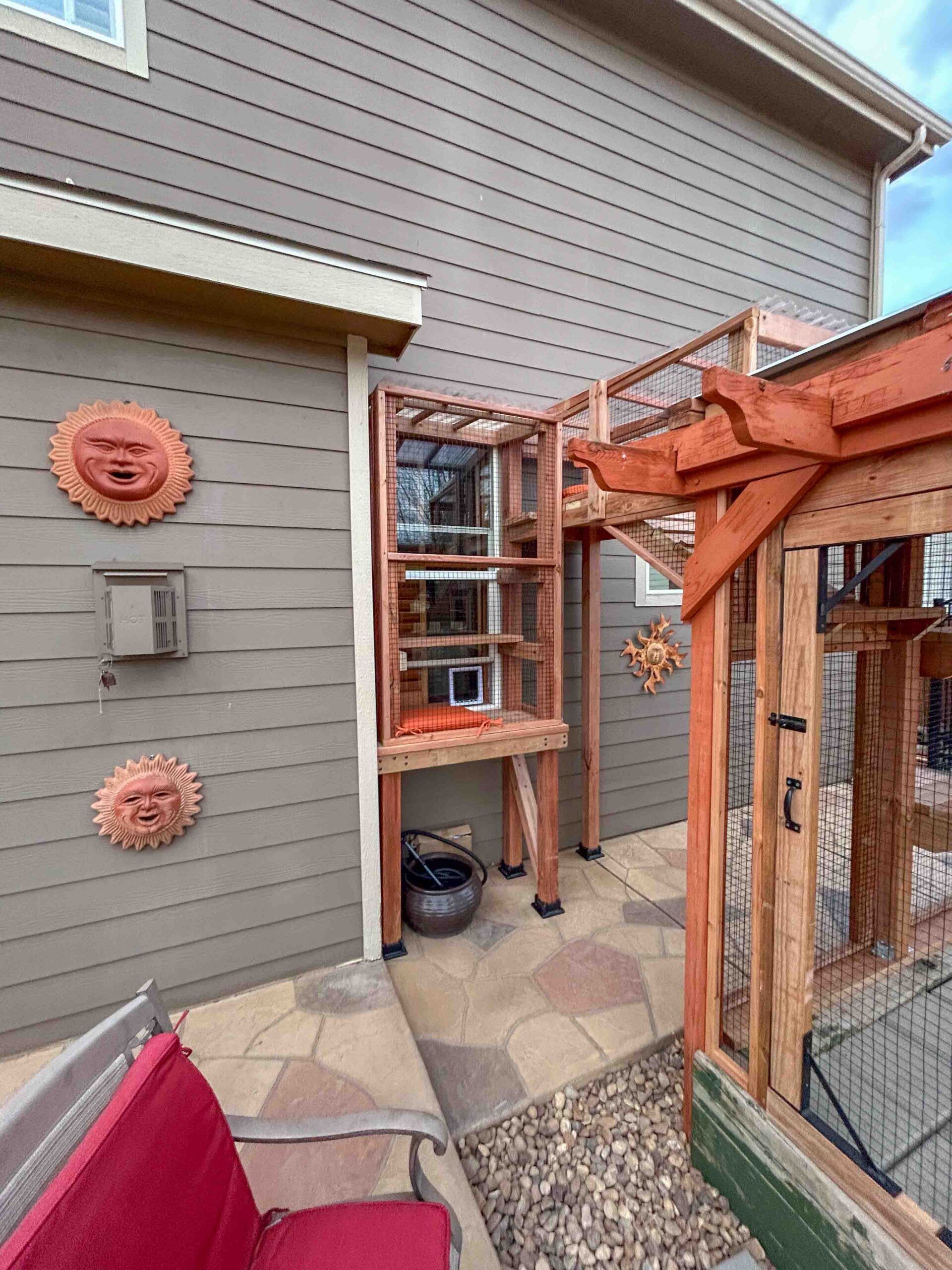 Vertical catio tower attached to exterior wall with multiple staggered shelves, cat window entry, and mesh enclosure providing safe outdoor access from inside the home.
