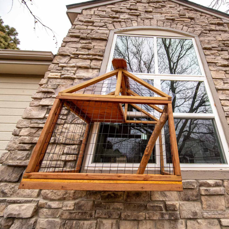 Wooden window-mounted catio with pitched roof attached to a stone exterior wall