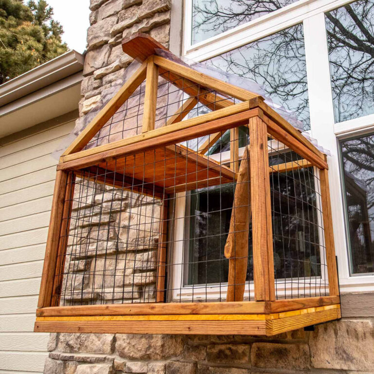 Close-up view of wooden catio with gable roof and natural branch support mounted on a stone house