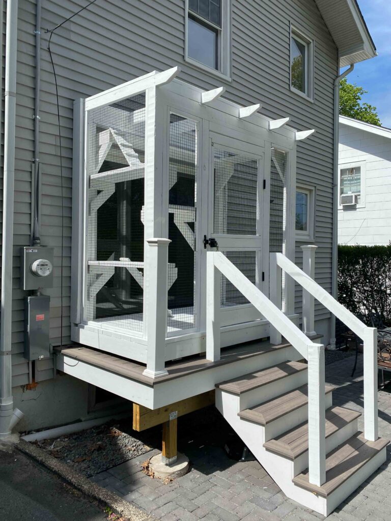 Side-angle view of a custom white catio in Glen Ridge, NJ, featuring mesh walls, decorative roof beams, and steps leading up to the structure.