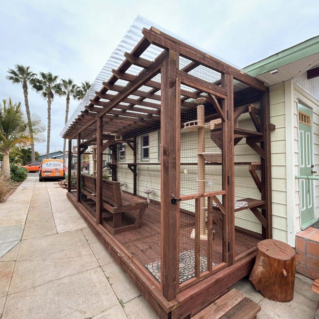 Large wooden catio attached to a house with a pergola-style roof, climbing shelves, sisal-wrapped post, and seating for humans.