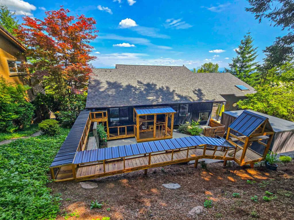 Expansive outdoor catio with multiple walkways, covered tunnels, and enclosures that wrap around a house and extend into a sloped backyard.