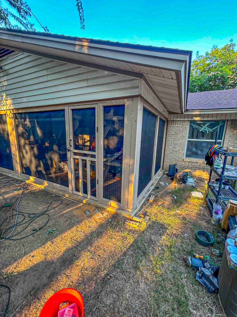 Angled view of a corner catio showcasing screened walls, sloped roofing, and a pet access door, integrated into the home’s exterior layout.