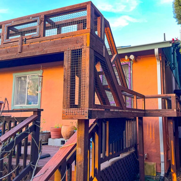 Elevated wooden catio tunnel attached to a home with orange siding, leading from the deck.