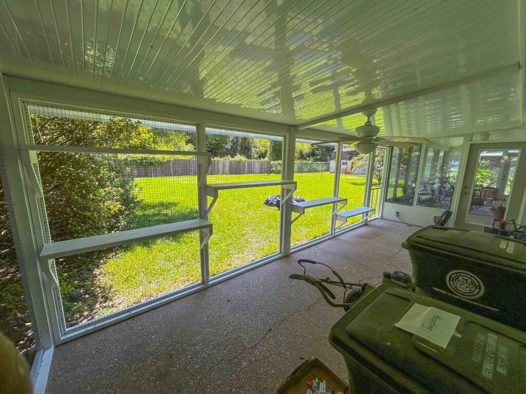 Interior view of a Baton Rouge catio with shelves, ceiling fan, and wide screened windows overlooking the backyard.