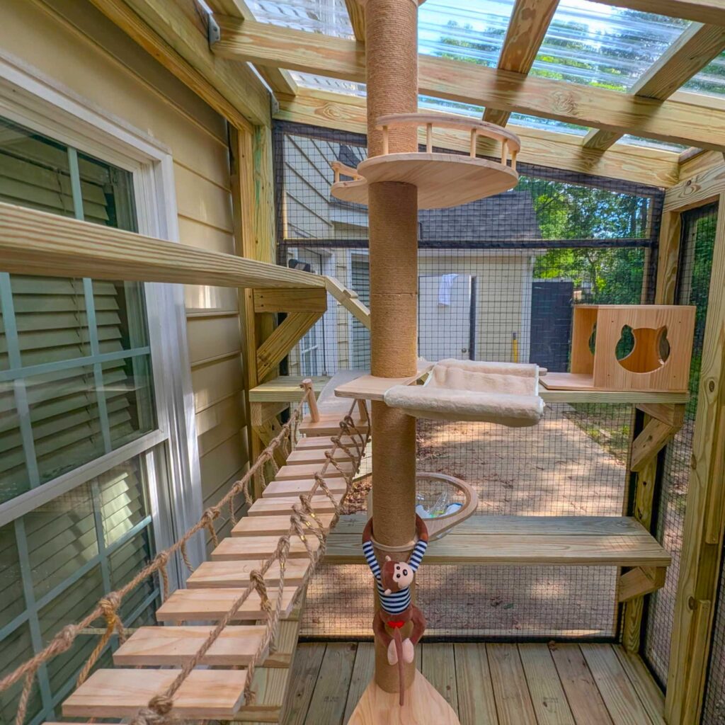 Custom catio interior with a central sisal-wrapped climbing post, hanging rope bridge, multiple platforms, and a cozy hammock for cats.
