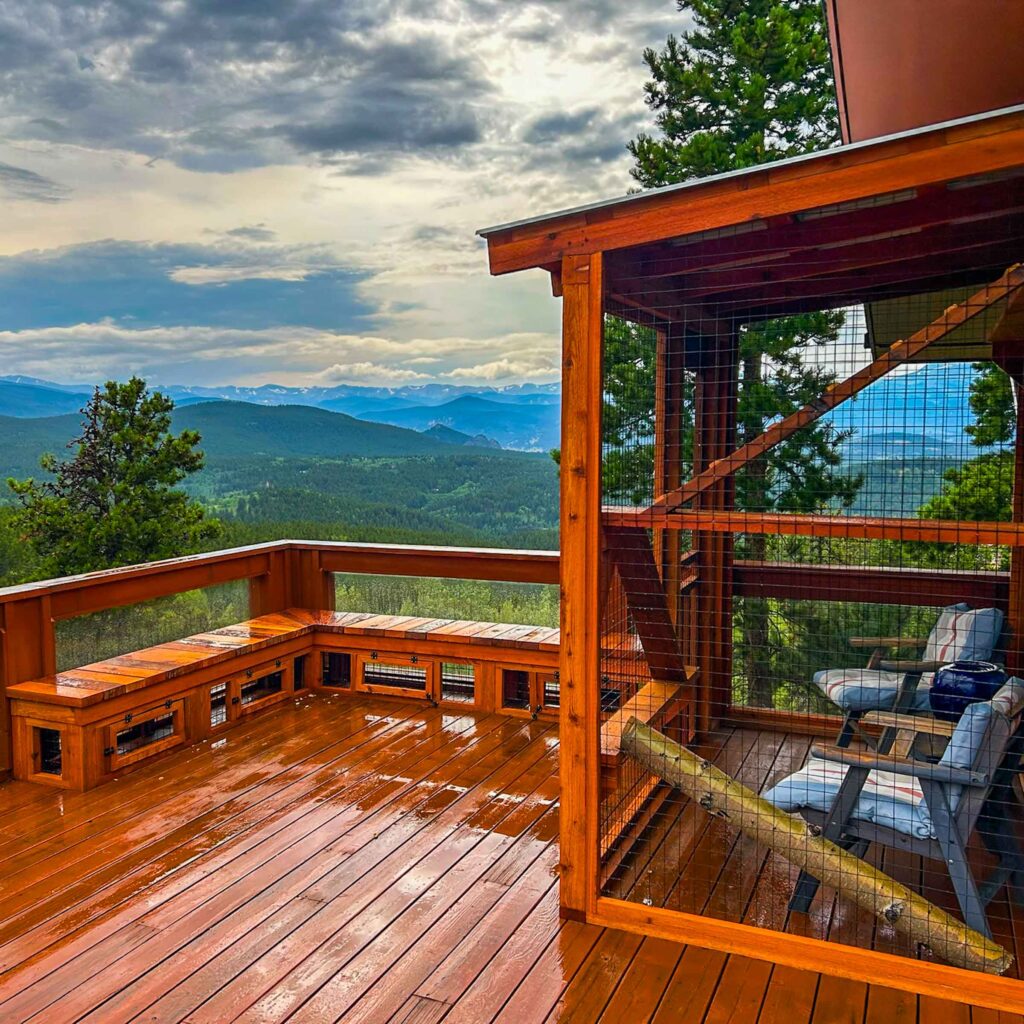 Large wooden catio enclosure on a deck with panoramic mountain views, featuring seating and a ramp inside.