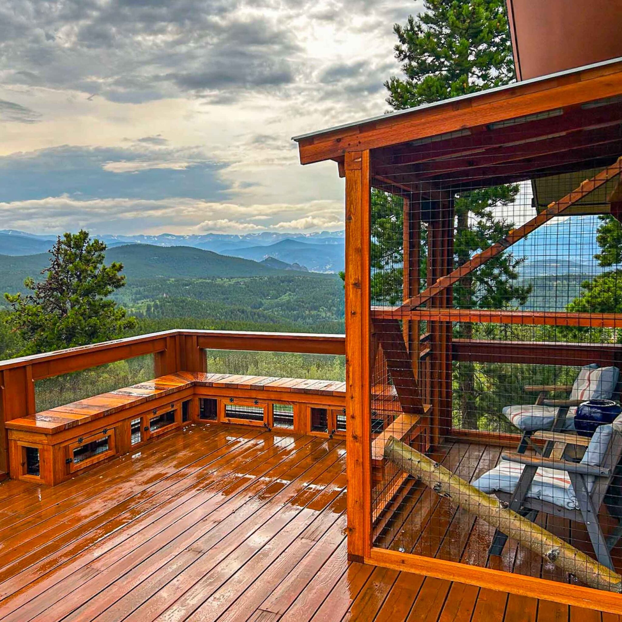 A large catio on a wooden deck with mesh walls, bench seating, and panoramic mountain views beyond the railing.