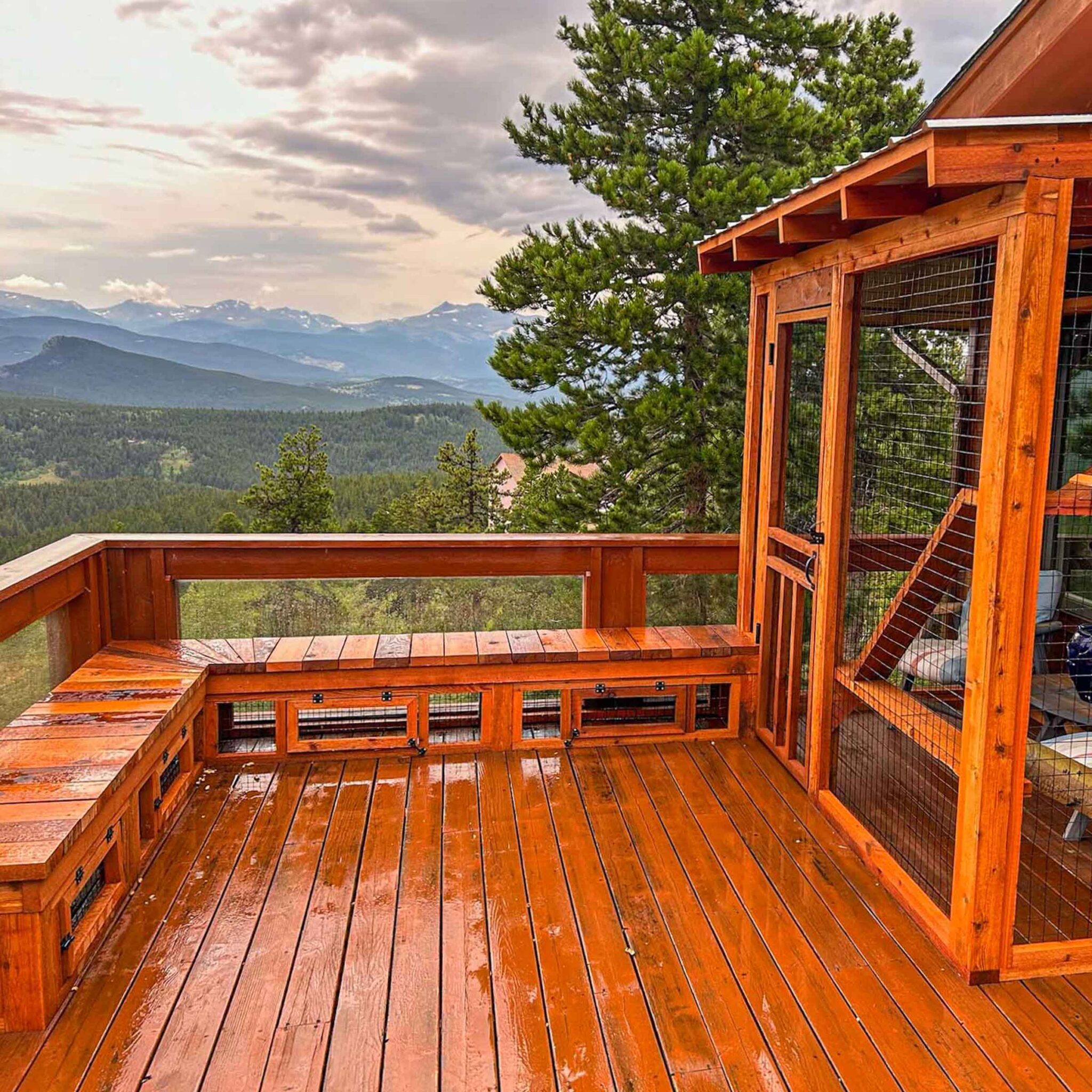 A catio with wet wooden decking and built-in benches, positioned on a balcony with sweeping mountain views.