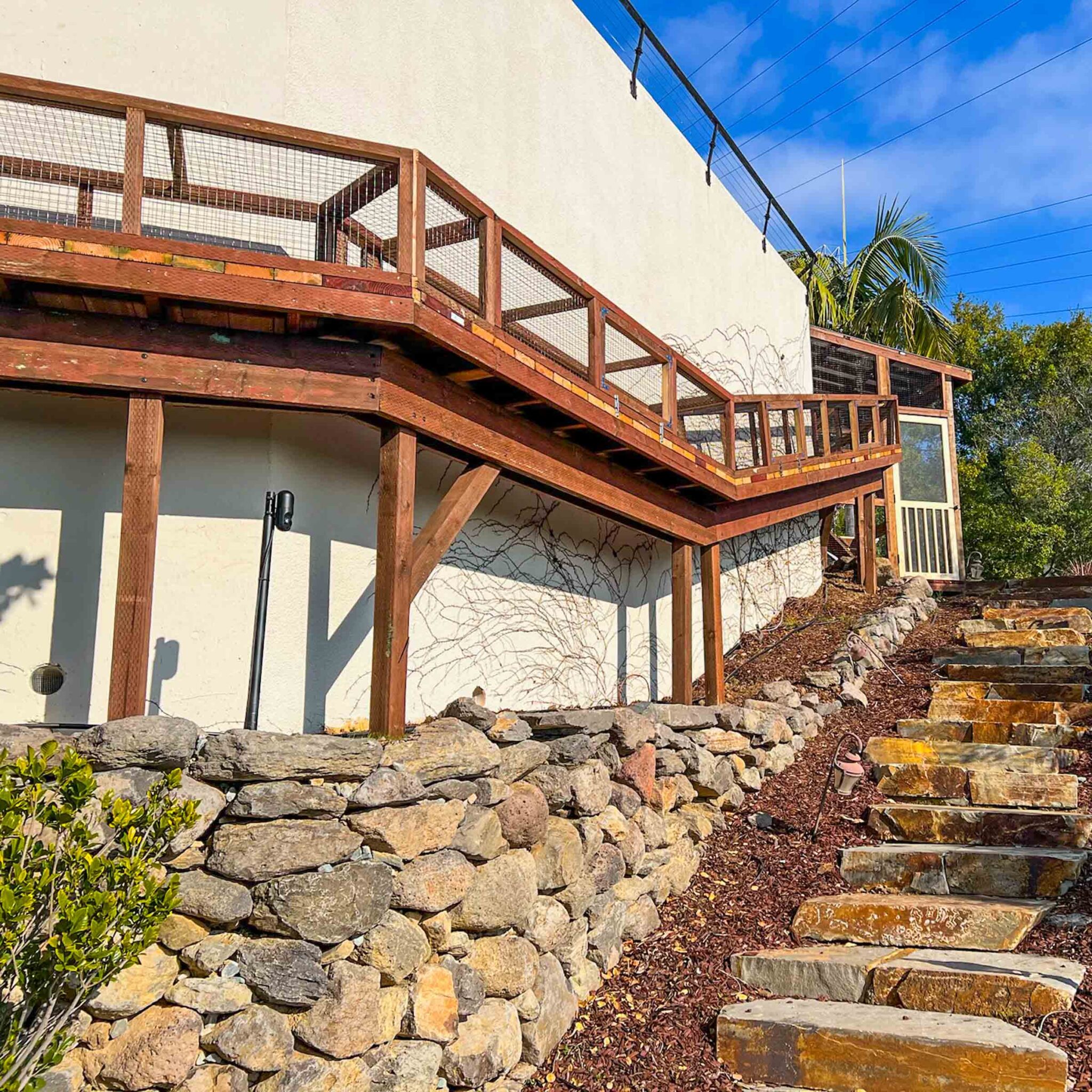 A hillside catio system with long elevated tunnels and a wooden enclosure at the base of a landscaped stone path.