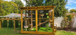 Large outdoor wooden catio with multiple climbing levels, hammocks, and a connecting tunnel leading from the house.