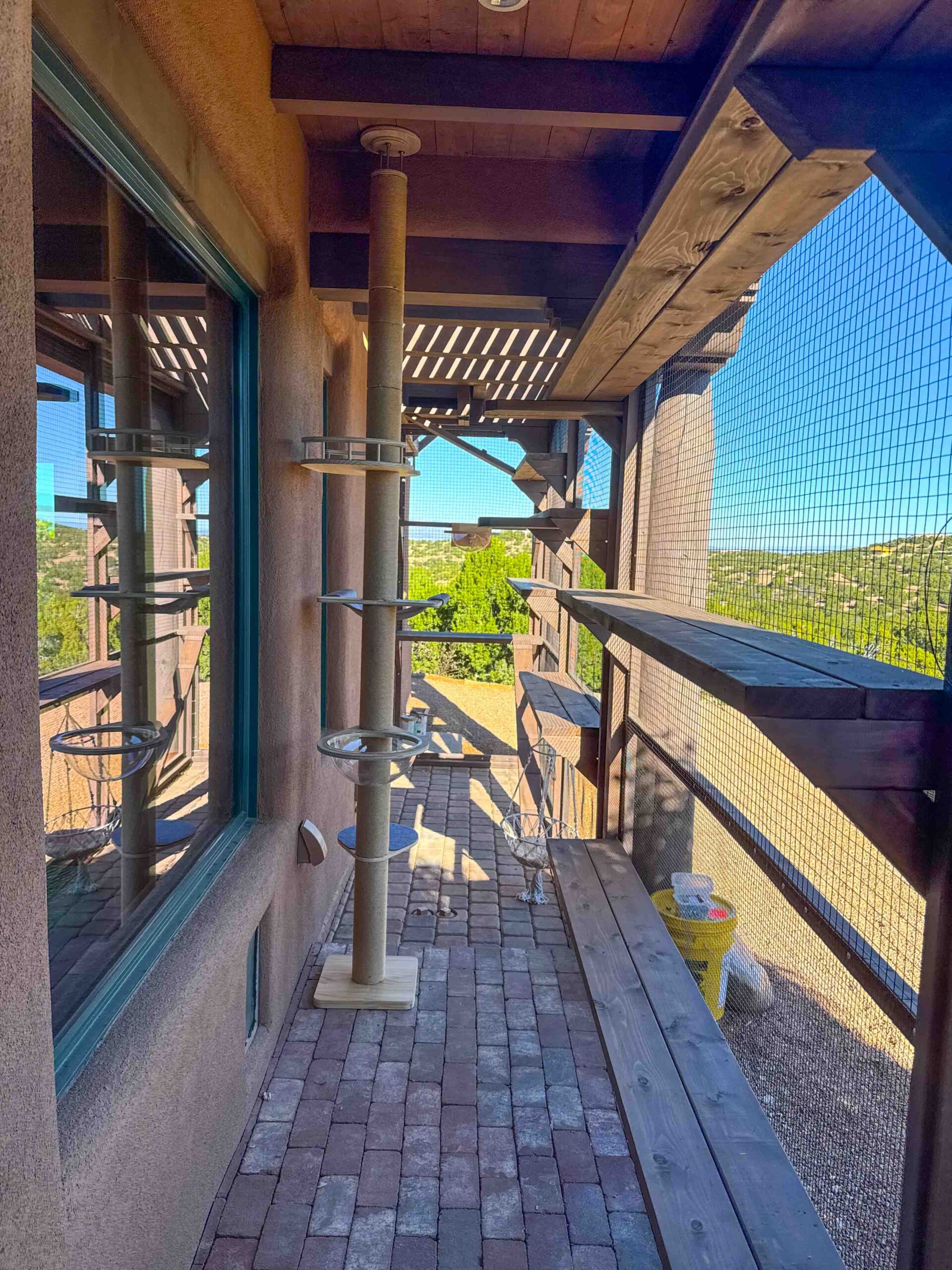 Long catio corridor with stained cedar platforms, a scratching post, and open hillside views.