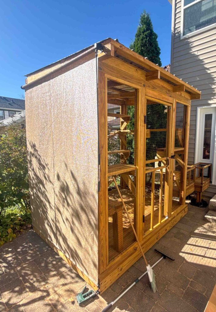 Wood-framed catio with mesh walls and retractable shade panels beside a Minneapolis home, featuring a man inspecting the finished build.