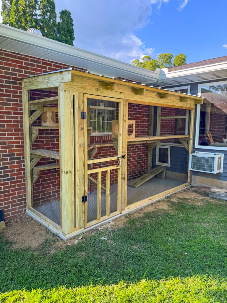 Side view of a custom wooden catio attached to a brick home in Sevierville, Tennessee, with multiple levels, ramps, and a screened door for cat access.