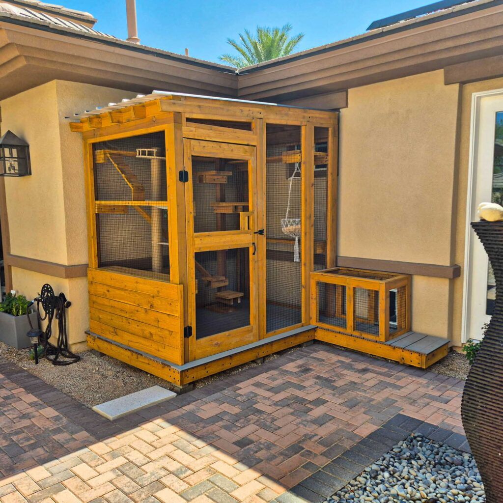 Compact wooden catio with connecting tunnel entry attached to a tan stucco home.