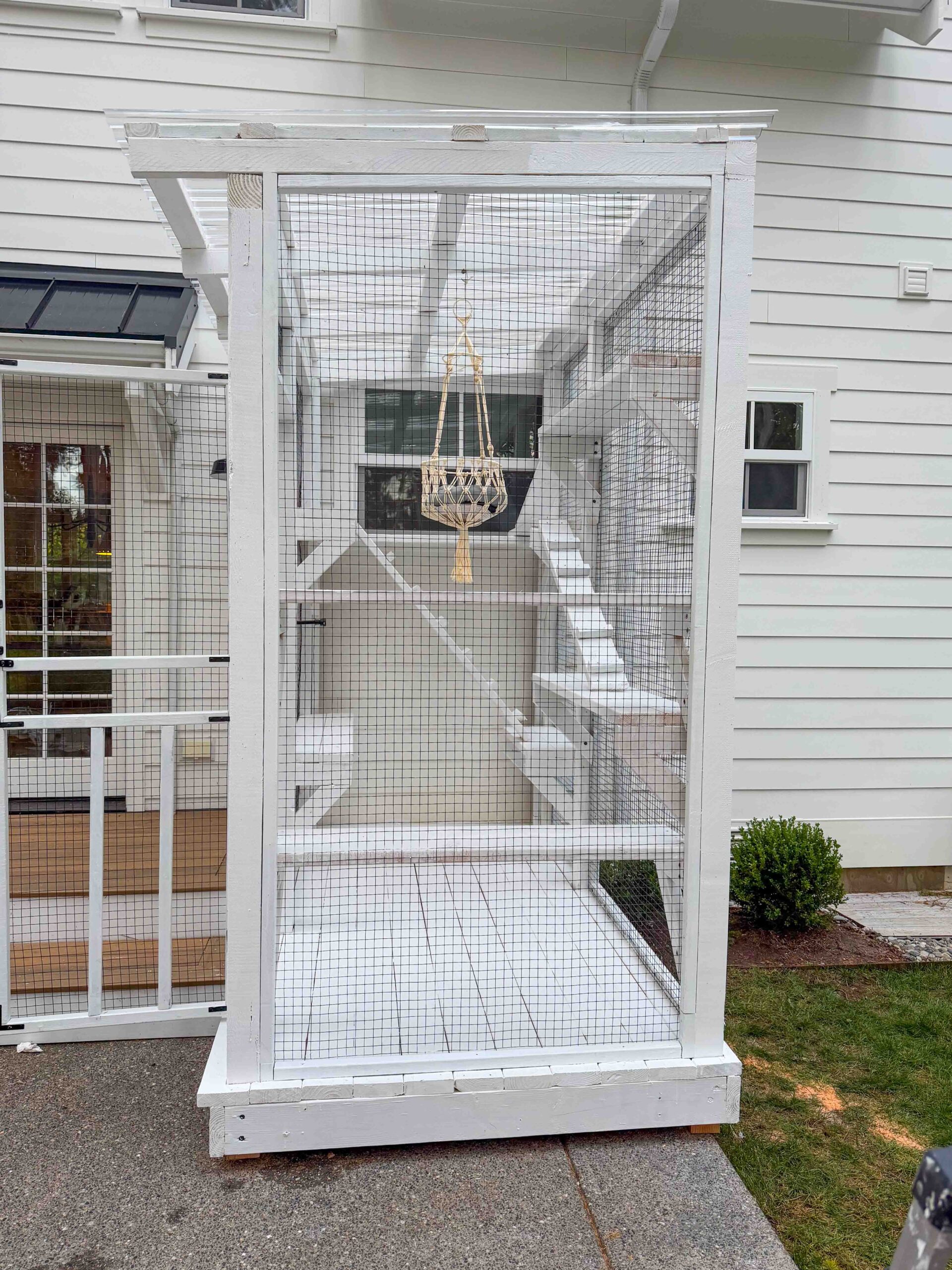 Custom white catio with elevated platforms and hanging basket attached to a modern white home.
