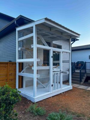 Angled view of a white custom-built catio connected to the side of a gray house.