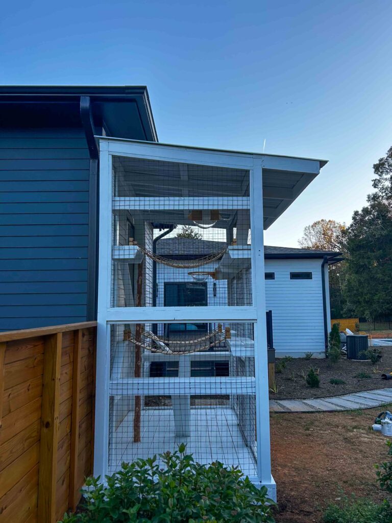 Side view of a tall white custom catio in Hillsborough, NC, showing interior cat hammocks, ramps, and secure mesh walls for outdoor play.
