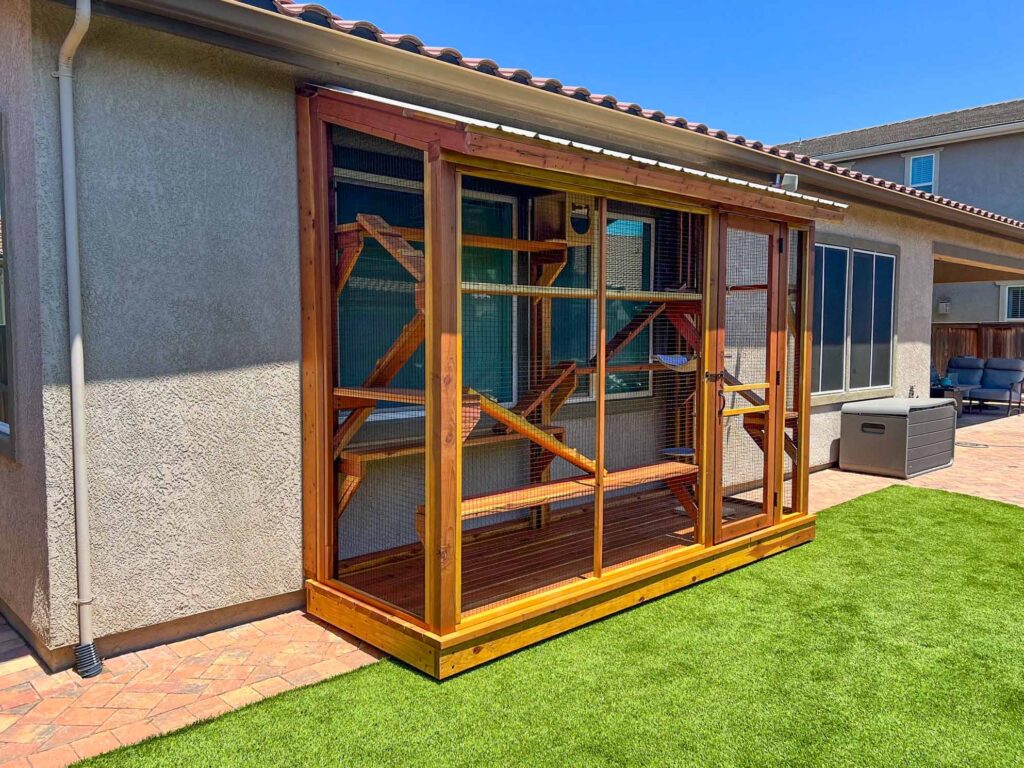 Long narrow wooden catio installed along a home exterior with interior ramps and shelves.