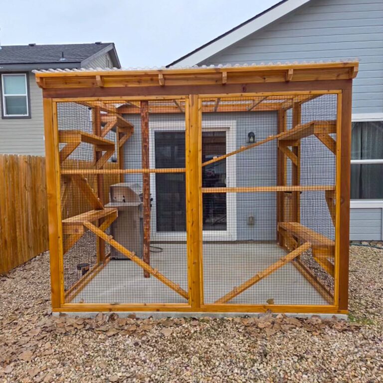 Front view of a custom wooden catio showing mesh walls, interior shelves, and a central log post.