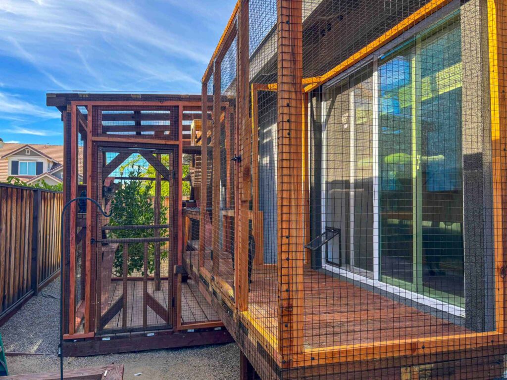 Wooden custom catio with an enclosed gate and mesh panels extending from a home.