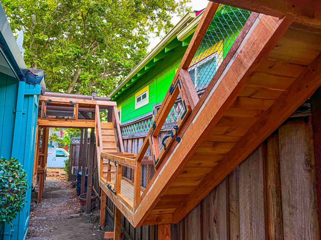 Elevated wooden catio ramp and enclosure system attached to a home with angled access panels.