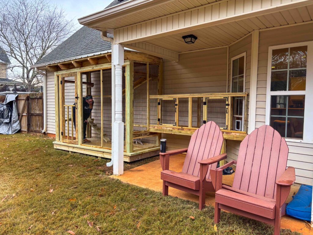 Custom catio connected to a home’s covered patio in McDonough, GA, with a builder inside and an elevated tunnel-style extension leading toward a window.
