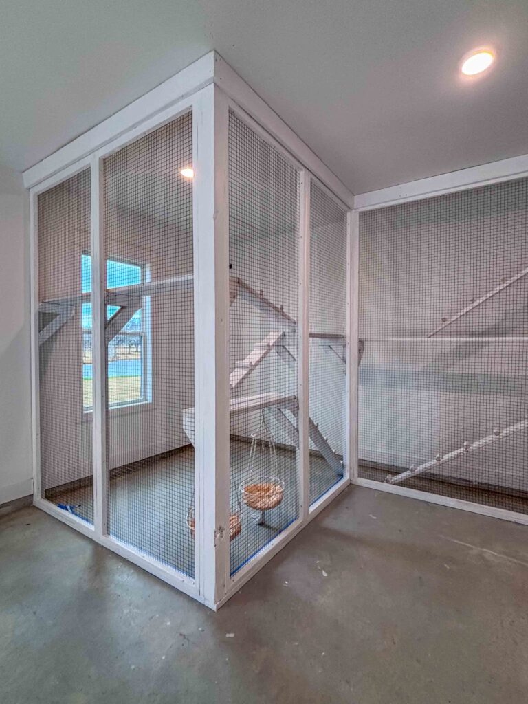 Corner view of a custom-built indoor catio in Dallas, GA featuring tall mesh walls, climbing ramps, shelves, and hanging basket beds.
