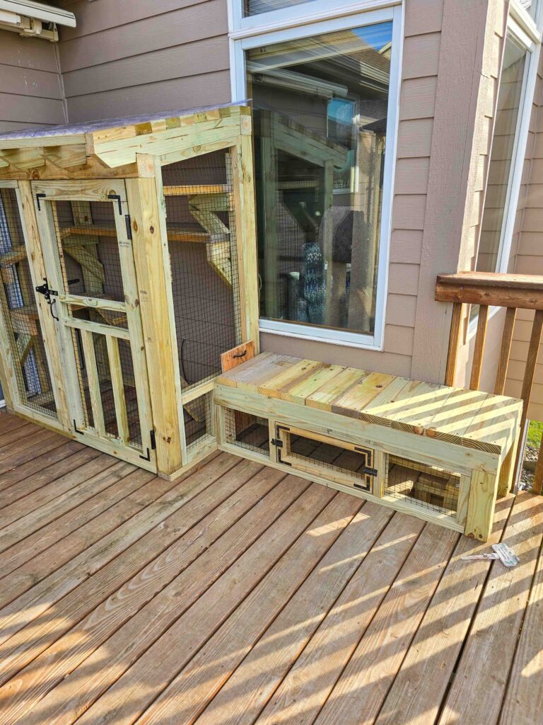 Custom-built window-entry catio with wood framing and secure wire mesh installed on a backyard deck in Ankeny, Iowa.