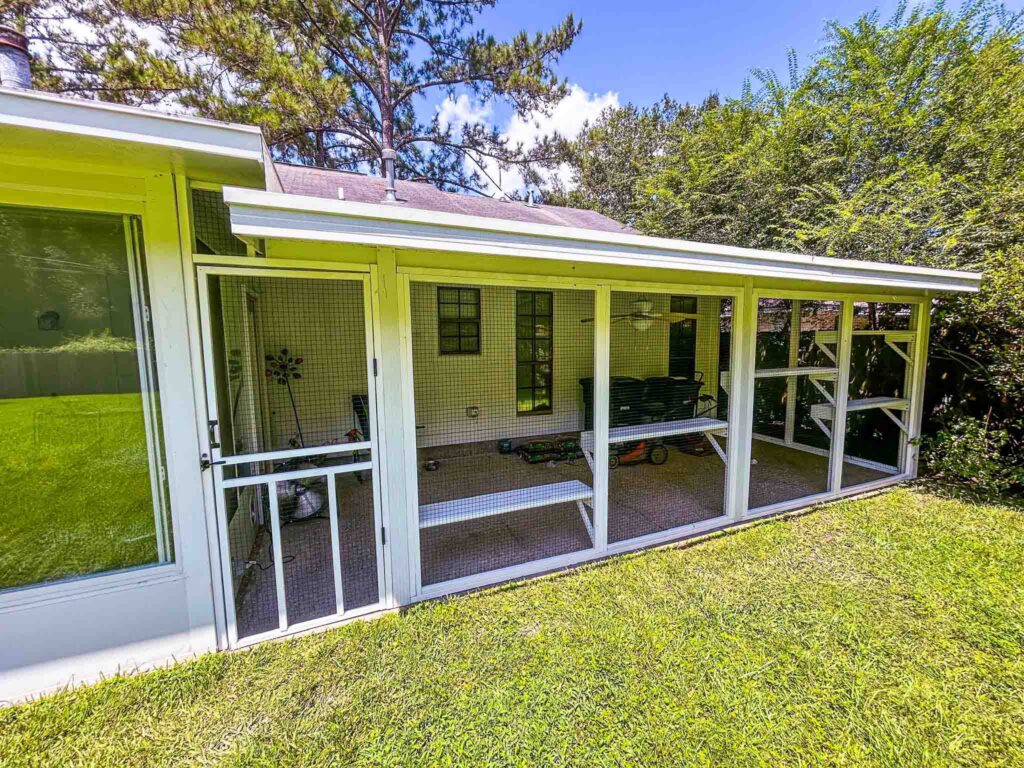 Long white custom catio enclosure attached to a screened porch with multiple access panels and shelves.
