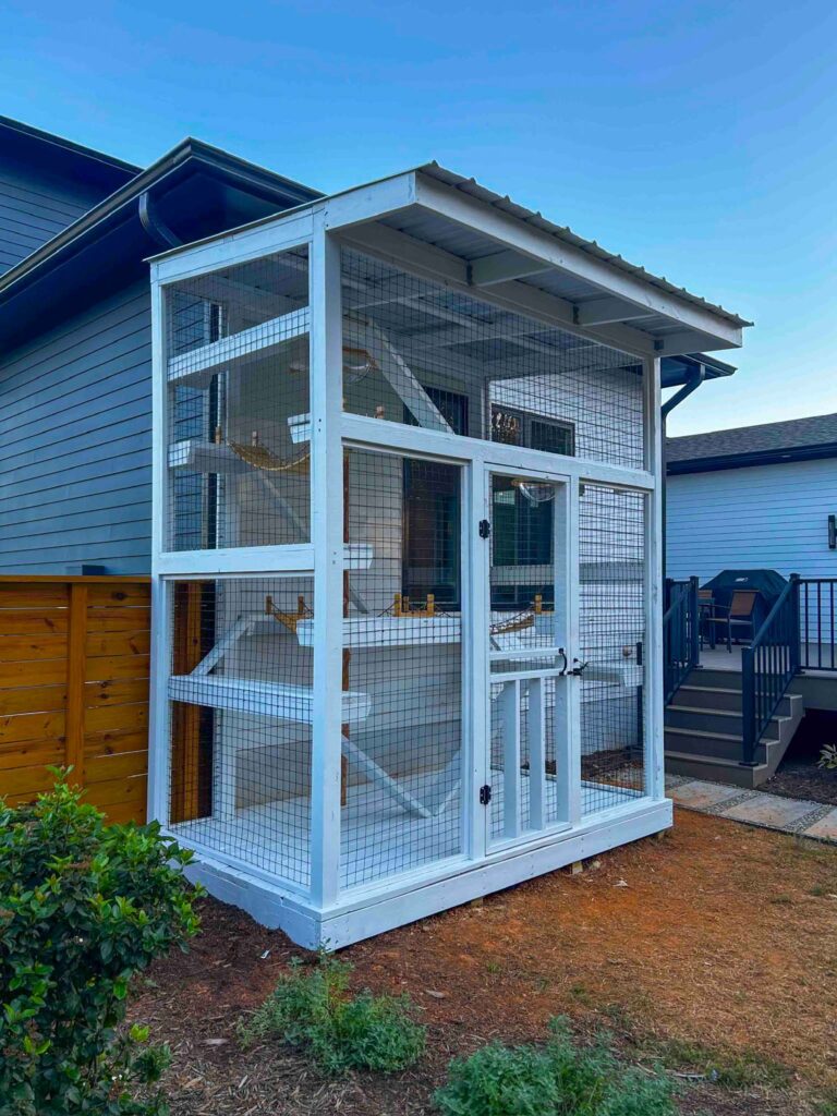 Tall white custom catio with multiple levels, ramps, and platforms built beside a modern home with a covered roof.