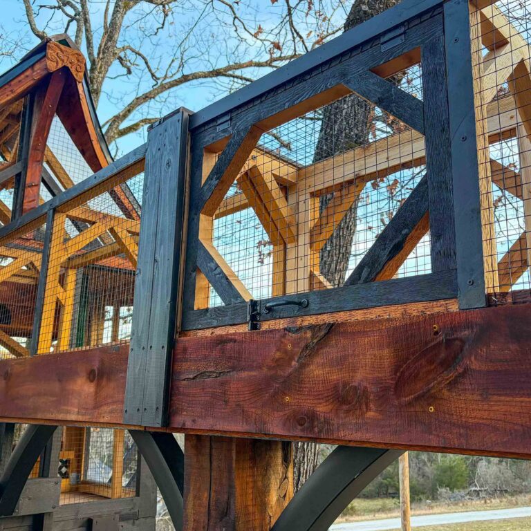 Close-up detail of handcrafted catio railing with geometric cross-bracing, black metal hardware, cedar planks, and tightly secured wire mesh panels on an elevated catwalk.