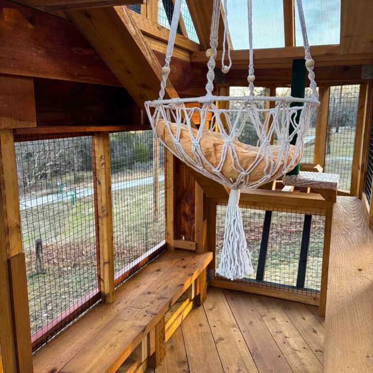 Close-up interior of elevated catio tower featuring cedar bench seating, wire mesh walls, translucent roofing panel, and suspended macrame hammock with cushion.