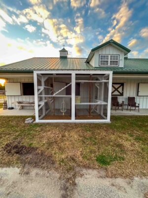 Front-facing view of a large two-section custom catio with symmetrical mesh panels, interior climbing structures, and vertical scratching posts attached to a farmhouse building.